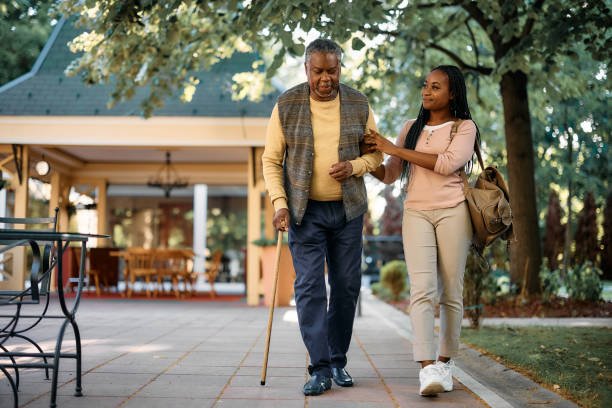 Smiling African American woman walking with her senior father while visiting him at nursing home.